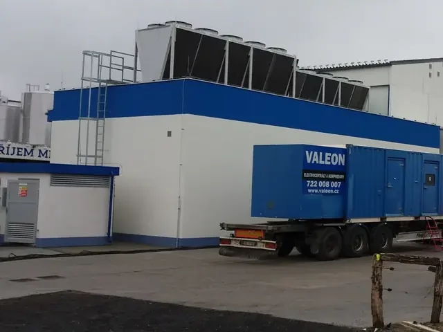 Kontejnerová centrála Valeon na návěsu u budovy mlékárny s chladicími jednotkami na střeše